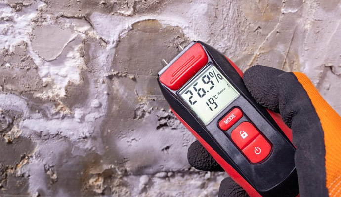 A moisture meter showing a high reading on a water-damaged wall